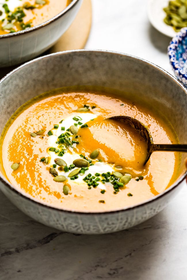 Carrot Ginger Soup garnished with creme fraiche and chives in a bowl with a spoon