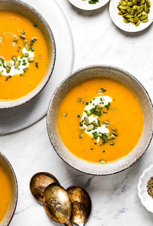 vegetarian carrot ginger soup in bowls garnished with pepitas and herbs