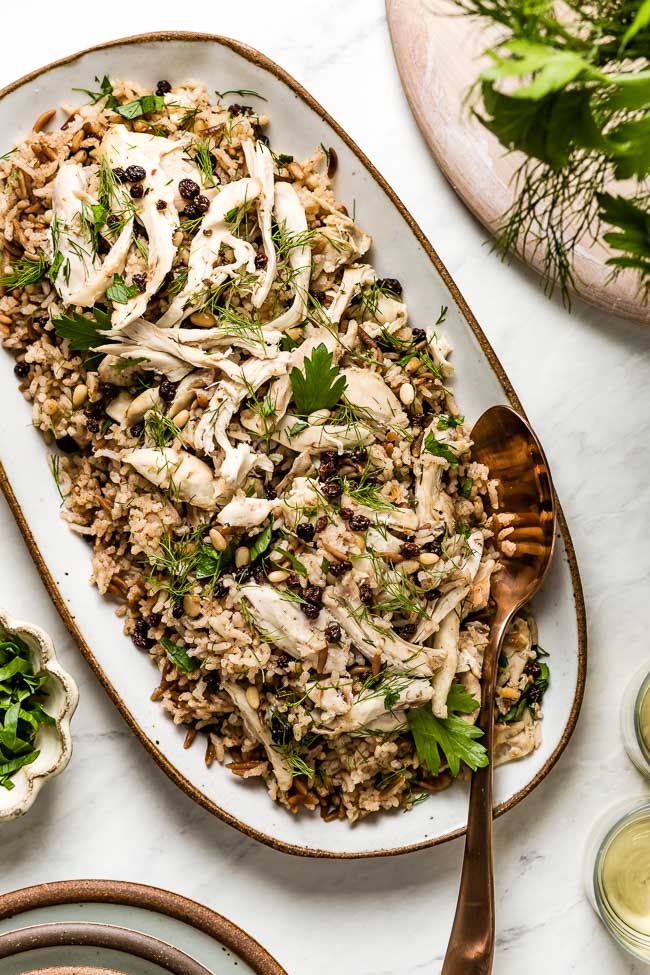 Chicken and Rice Pilaf garnished with fresh herbs on an oval plate with a spoon on the side.
