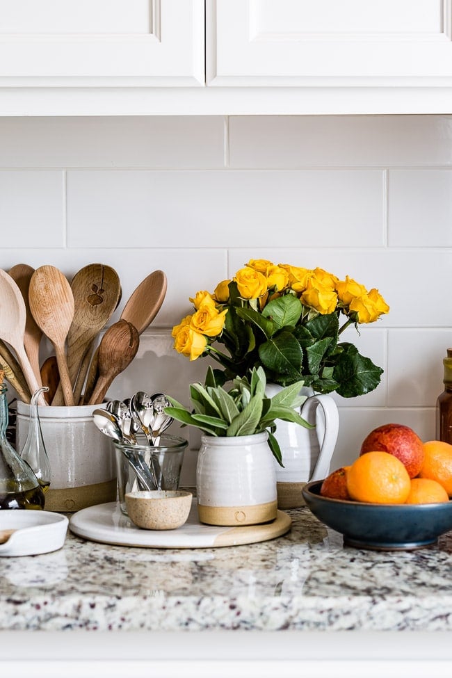 A kitchen counter with white pottery and yellow roses