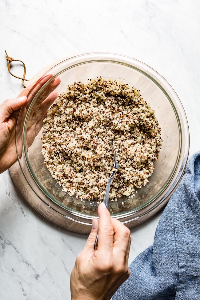 Quinoa cooked in microwave is in a bowl. A woman is fluffing it with a fork.