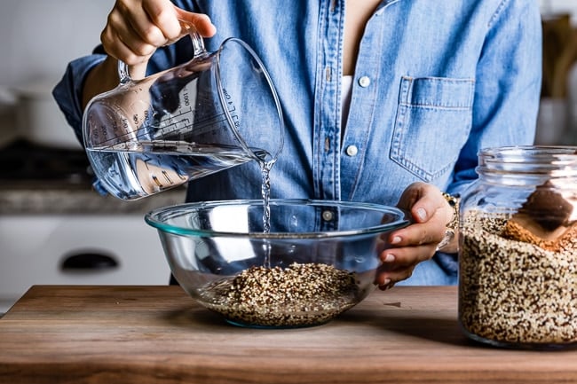 person pouring water into a cup with quinoa