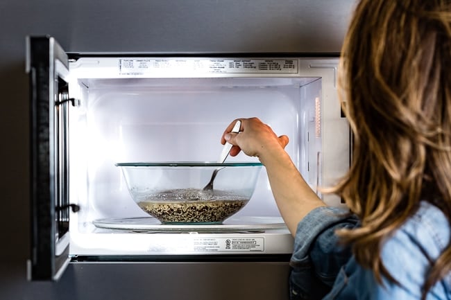 Person mixing quinoa in microwave in between cooking 