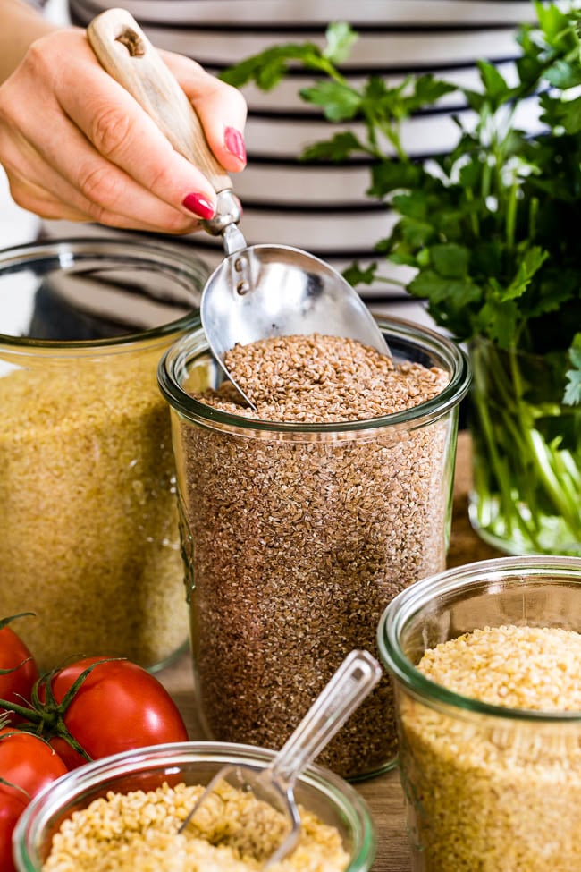 Person scooping red bulgur in a jar