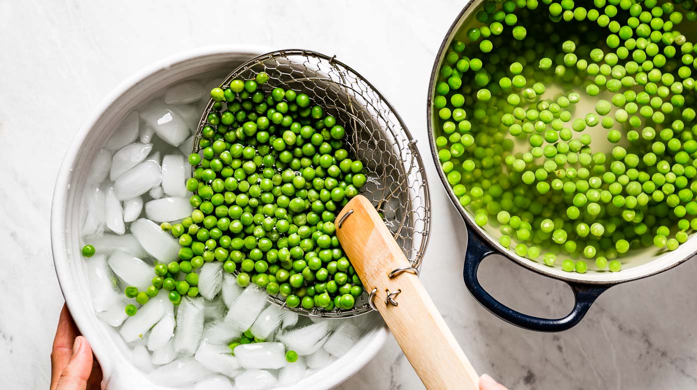 Person transferring blanched peas into a bowl with ice water