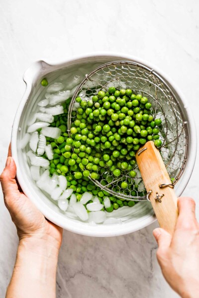 Person placing blanched peas into bowl with ice water