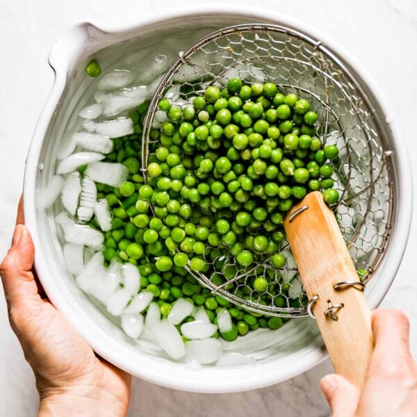 Person placing blanched peas into bowl with ice water