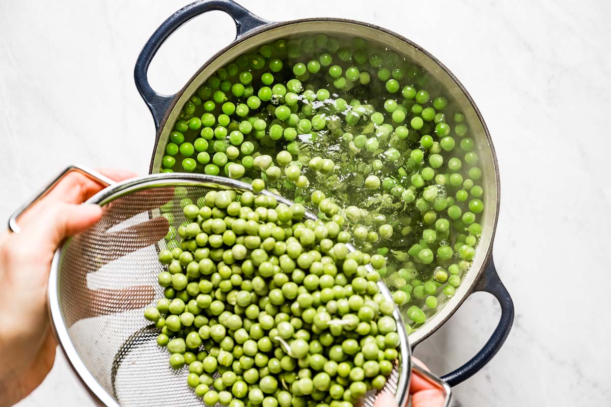Person placing fresh peas into a pot with boiling water