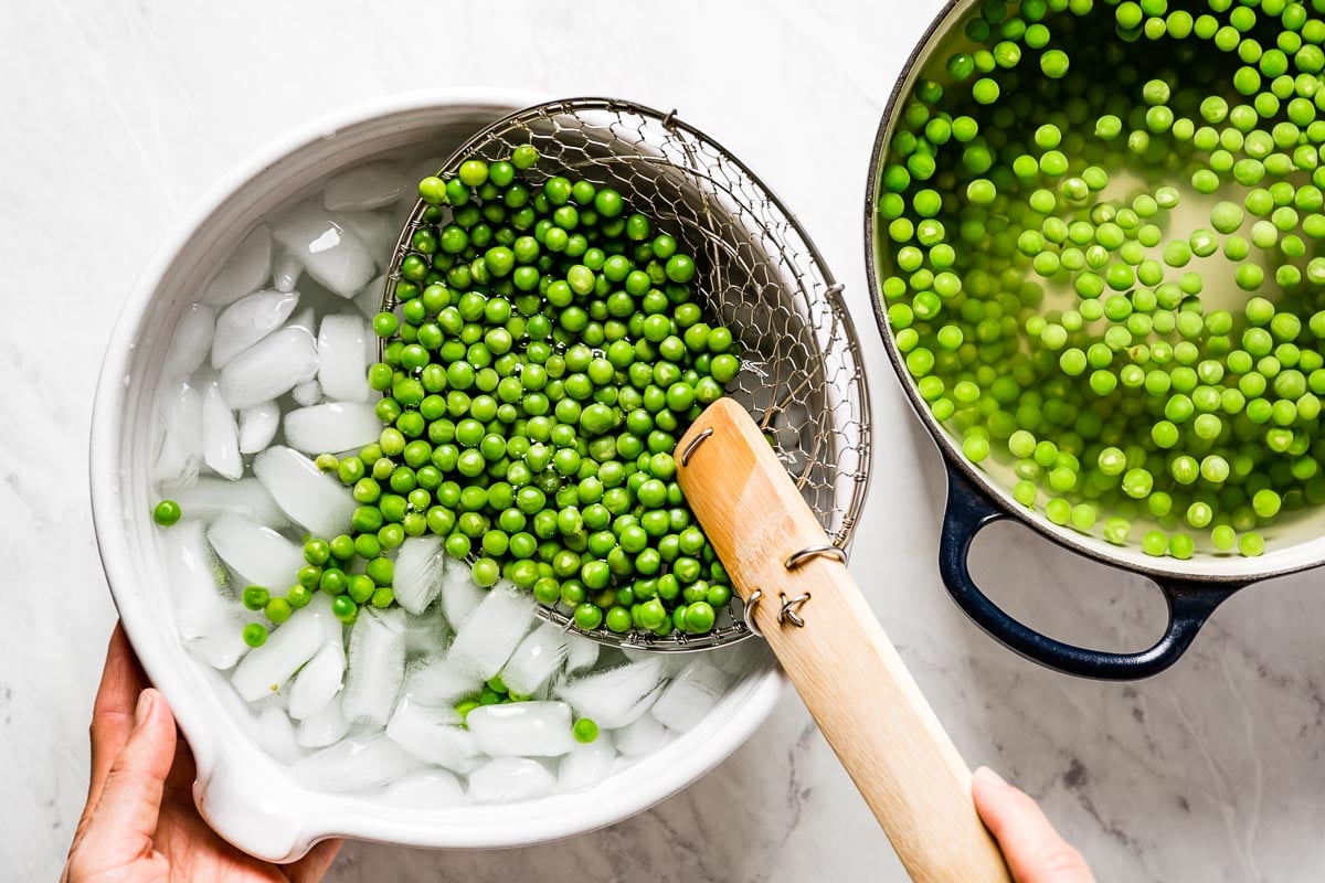 person placing blanched peas in a bowl of ice water
