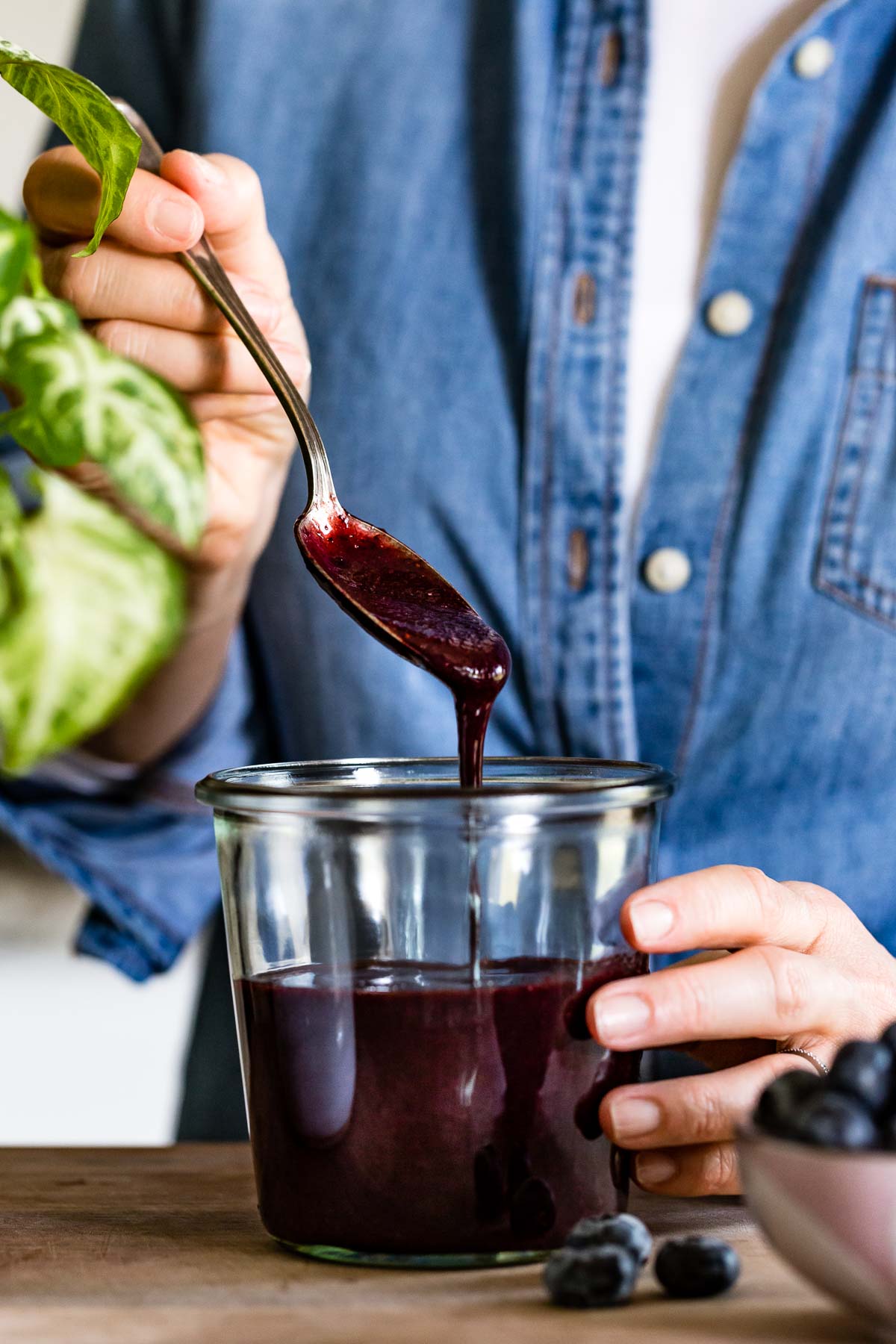 Blueberry puree is placed in a jar by a person