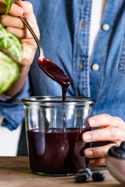 Blueberry puree is being placed in a jar by a person