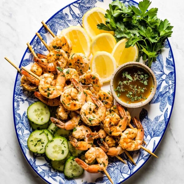 Grilled shrimp skewers on a plate with lemon, herbs and cucumber slices