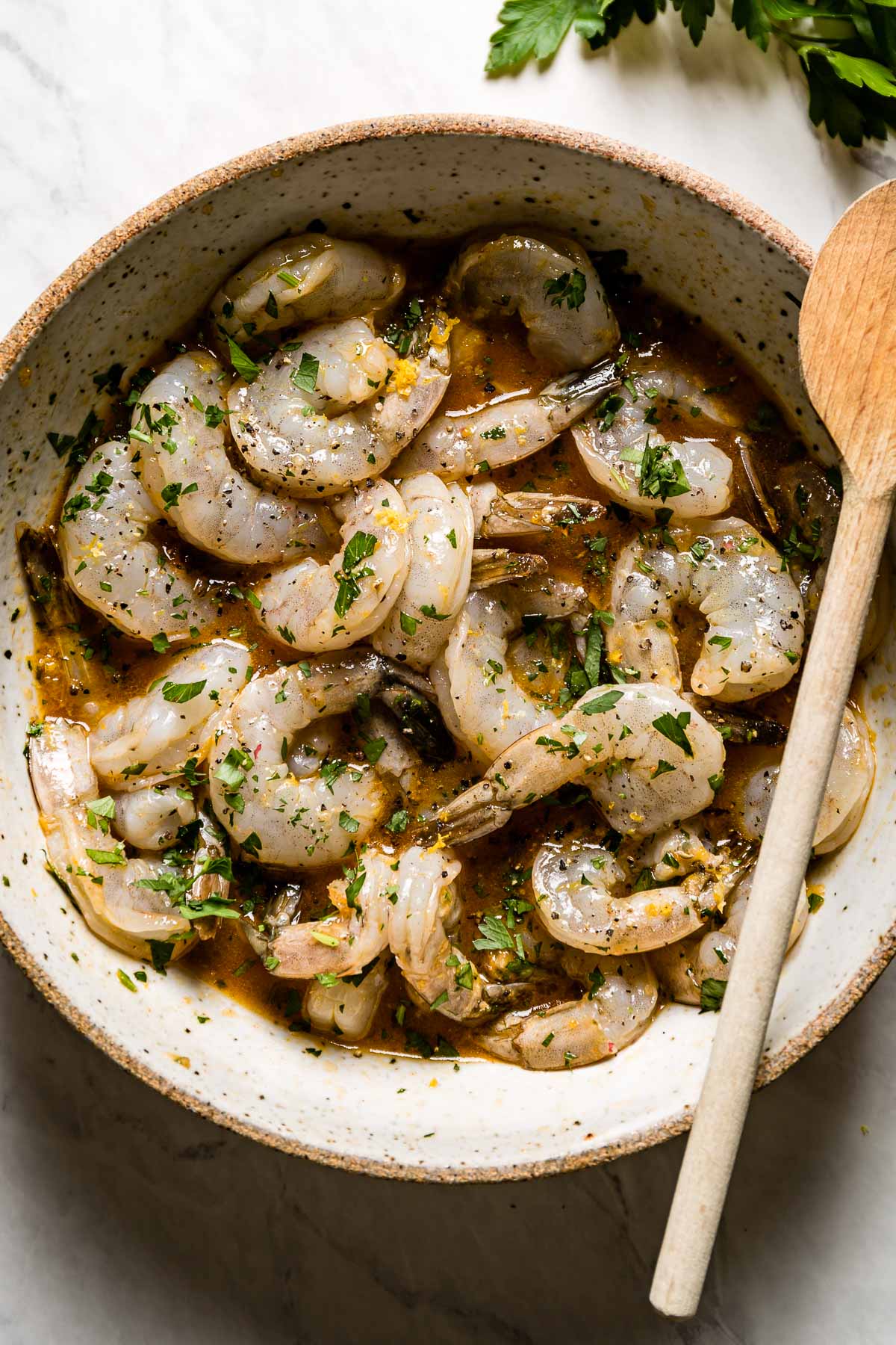 Shrimp marinading in a bowl with a wooden spoon on the side