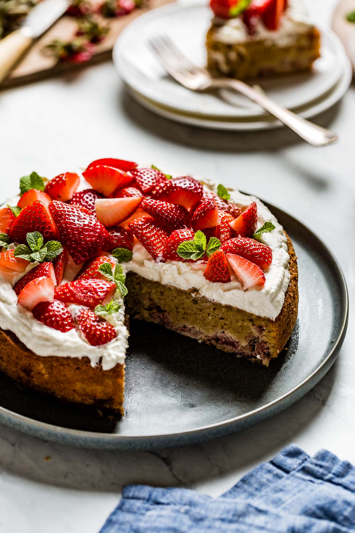 strawberry almond cake is served on a plate with a slice on a plate in the background