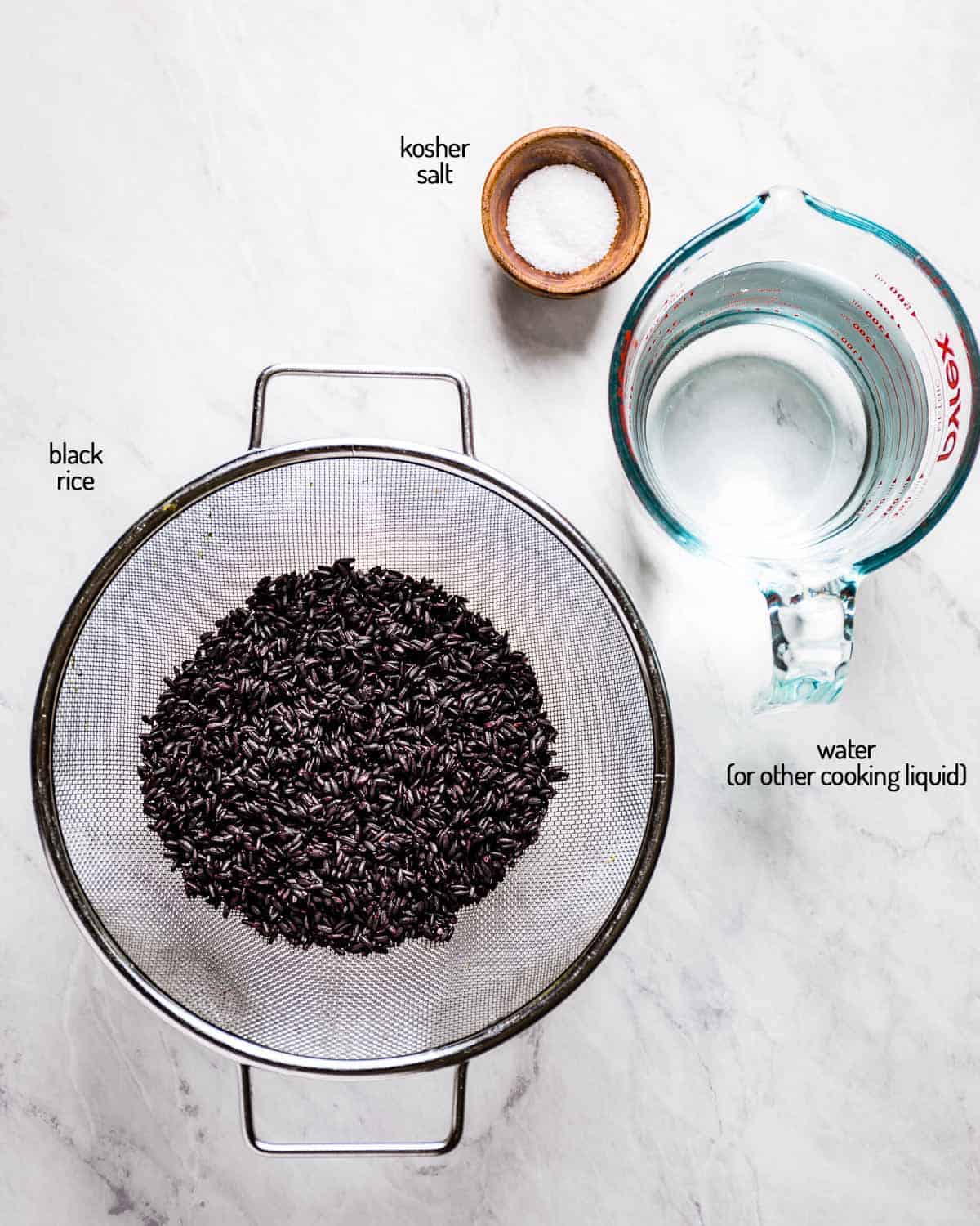 Ingredients for cooking black rice laid out on a white backdrop