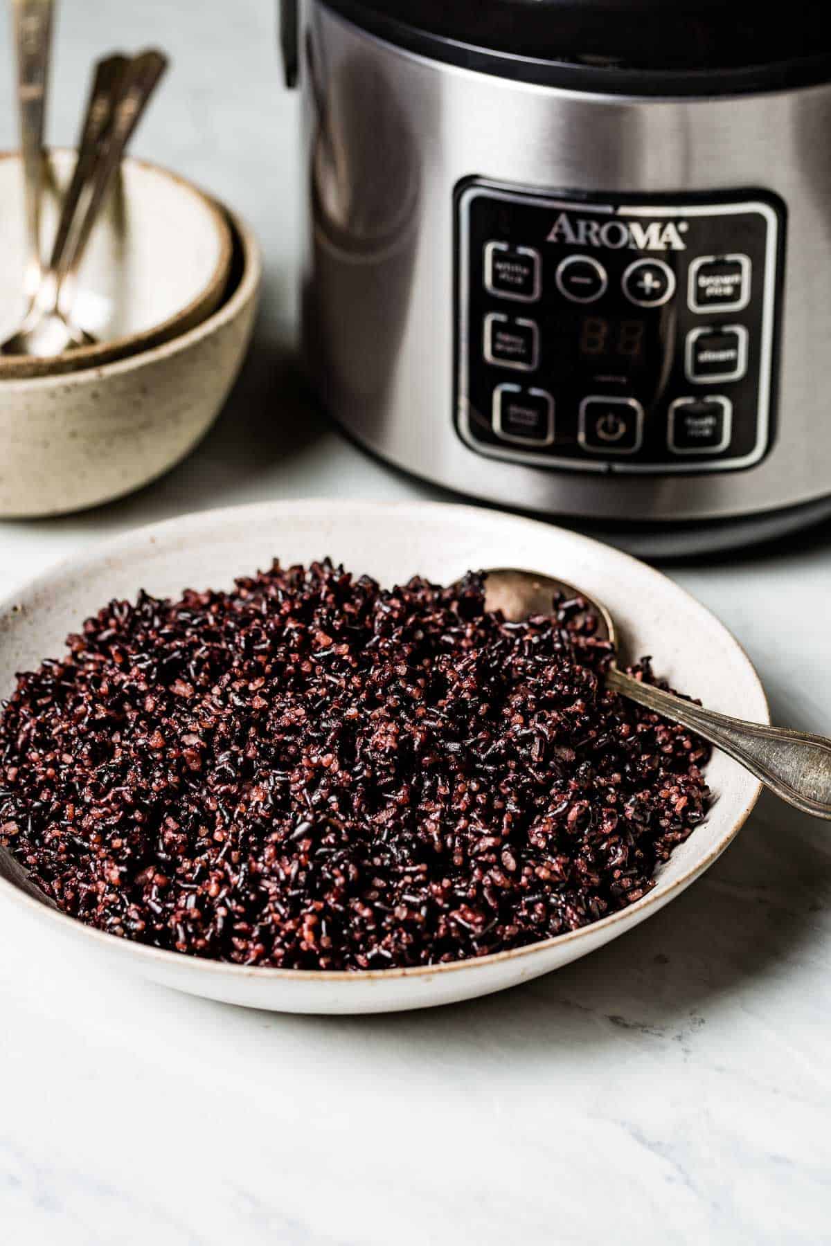 A bowl of cooked forbidden rice in front of an aroma rice cooker