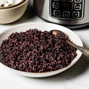 A bowl of cooked black rice in front of a rice cooker