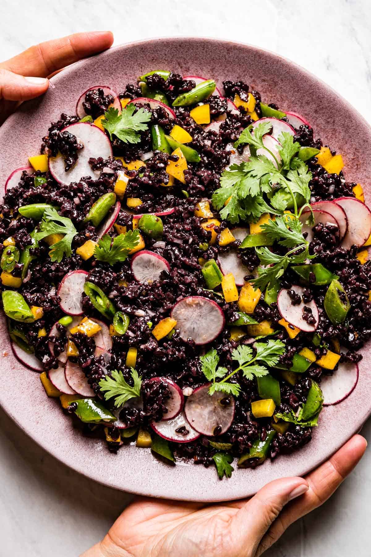 Black rice salad served on a pink plate by a person from top view