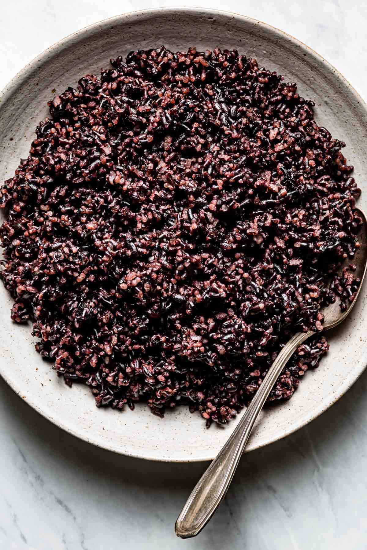 A bowl of purple rice in a bowl with a spoon on the side