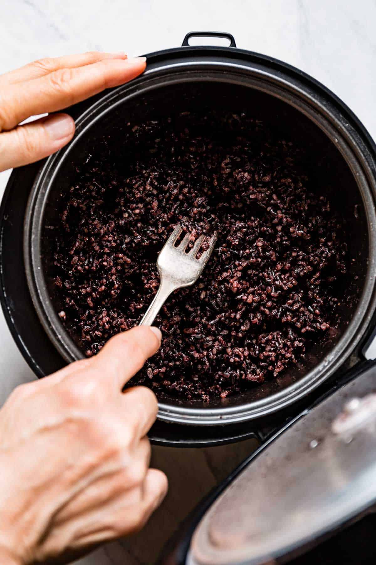 person fluffing cooked purple forbidden rice in a rice cooker