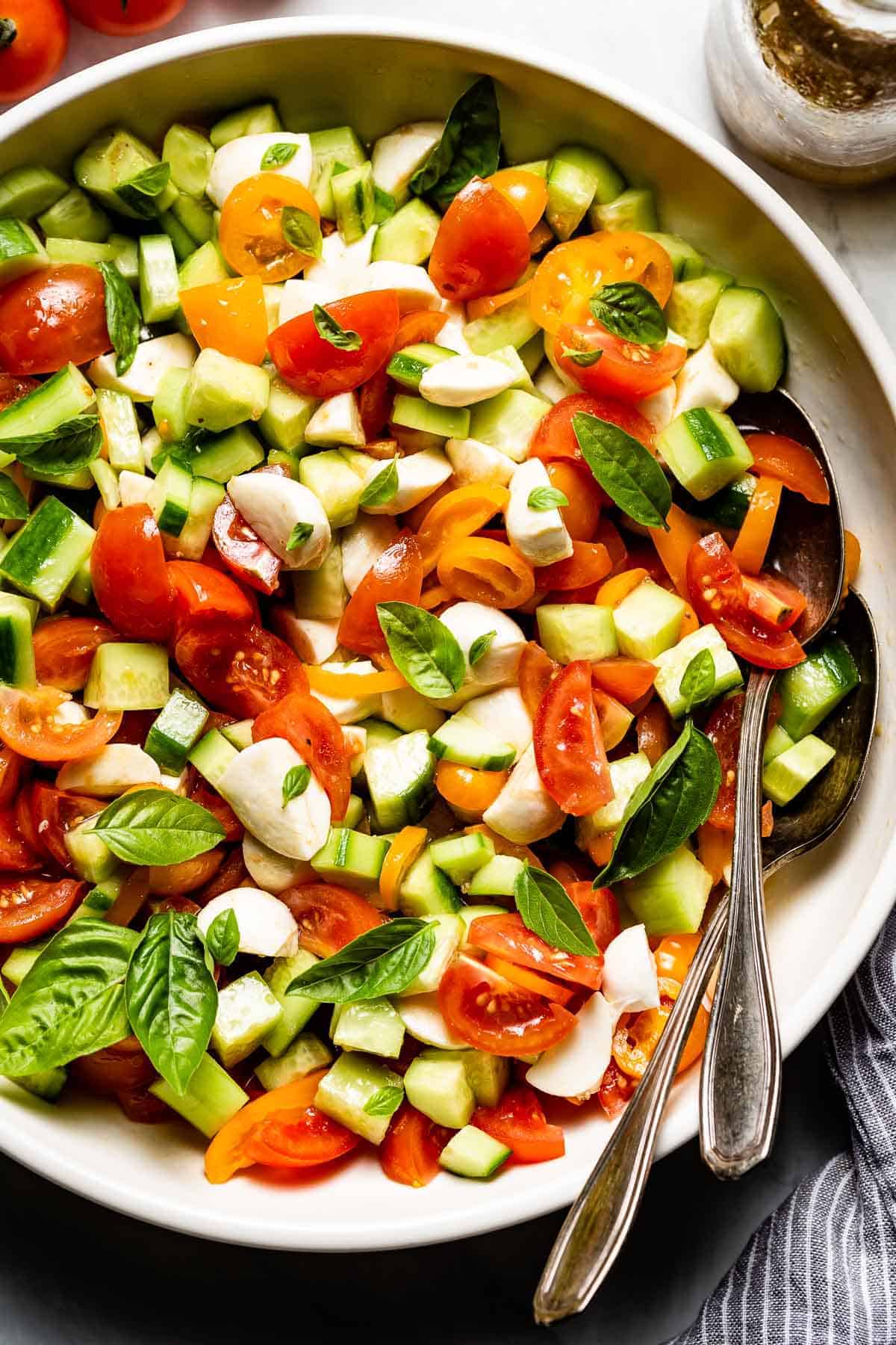 Cucumber Tomato Mozzarella Salad in a bowl with spoons on the side