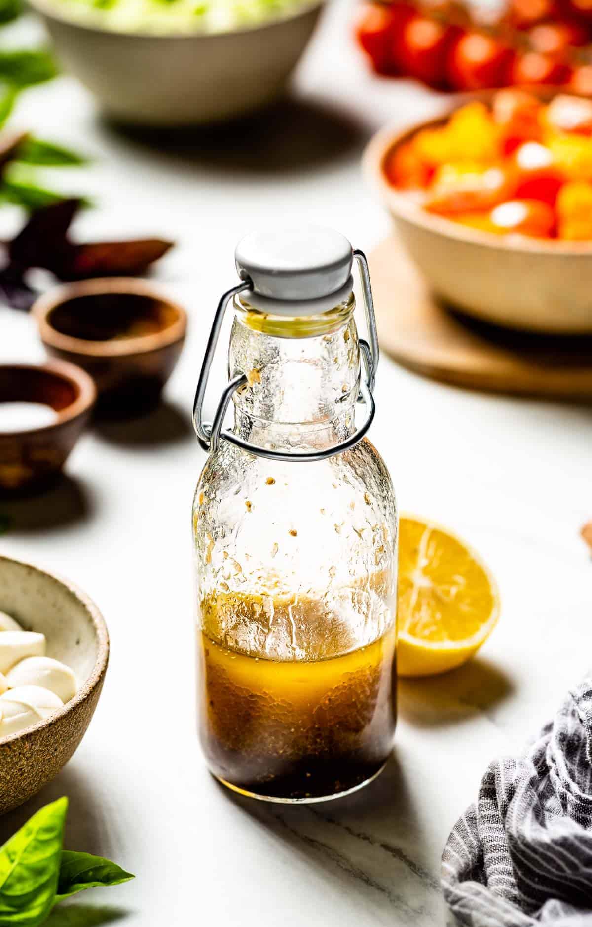 lemon balsamic vinaigrette placed in a bottle with salad ingredients around it.