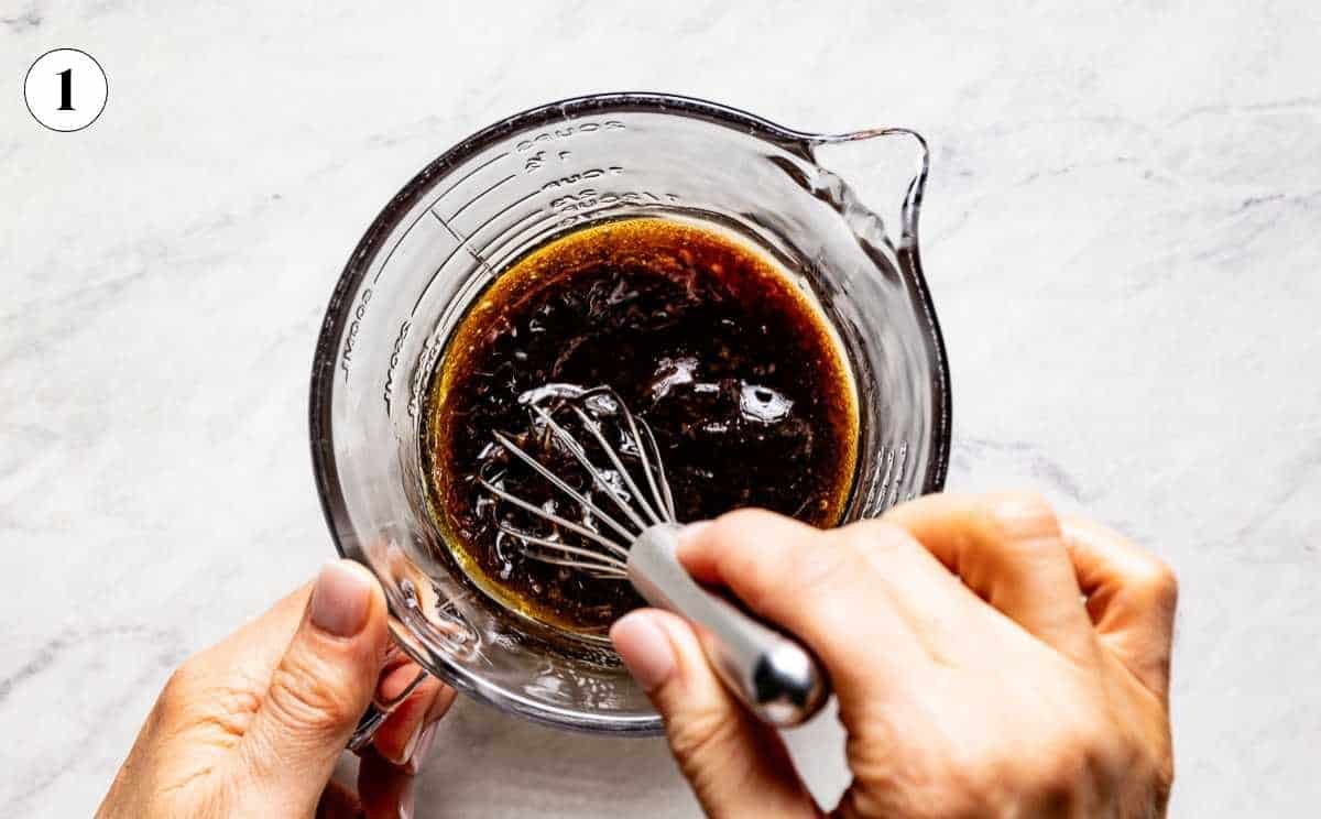 Hands whisking balsamic lemon dressing in a glass measuring cup for a spinach blueberry salad.