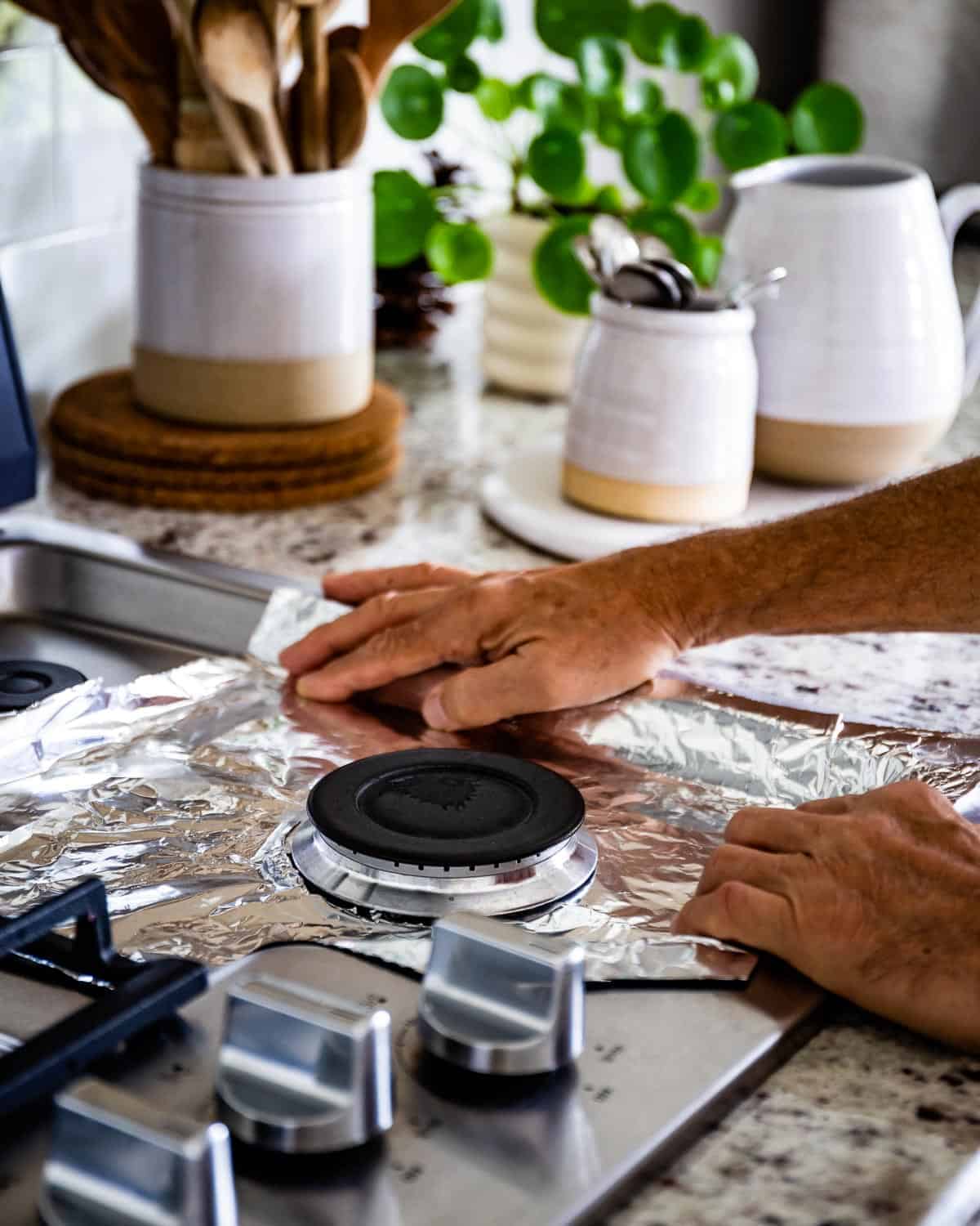 Person laying the bottom of a stove with aluminum foil