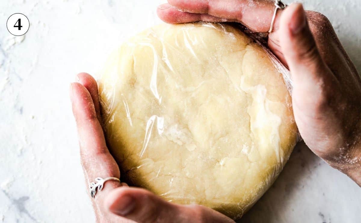 Hands holding the galette dough shaped into a disk and wrapped in plastic, ready to chill.