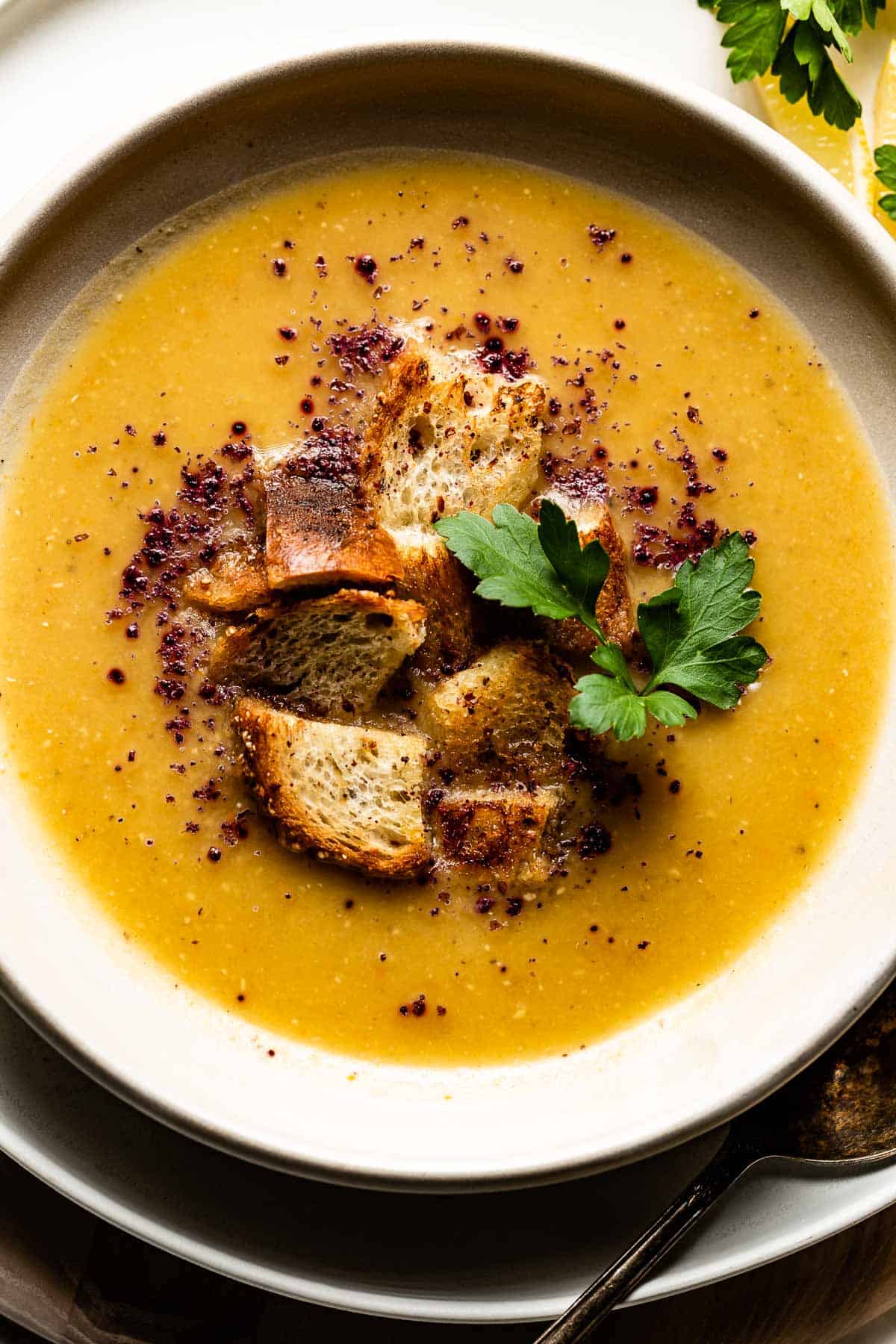 Turkish red lentil soup in a bowl topped off with croutons, sumac, and parsley.