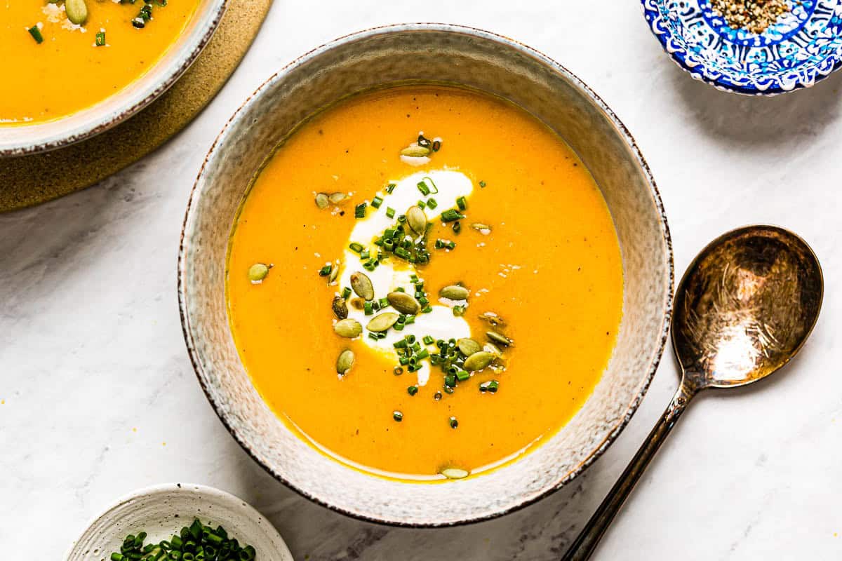 Creamy carrot ginger soup garnished with pumpkin seeds in a bowl from the top view.