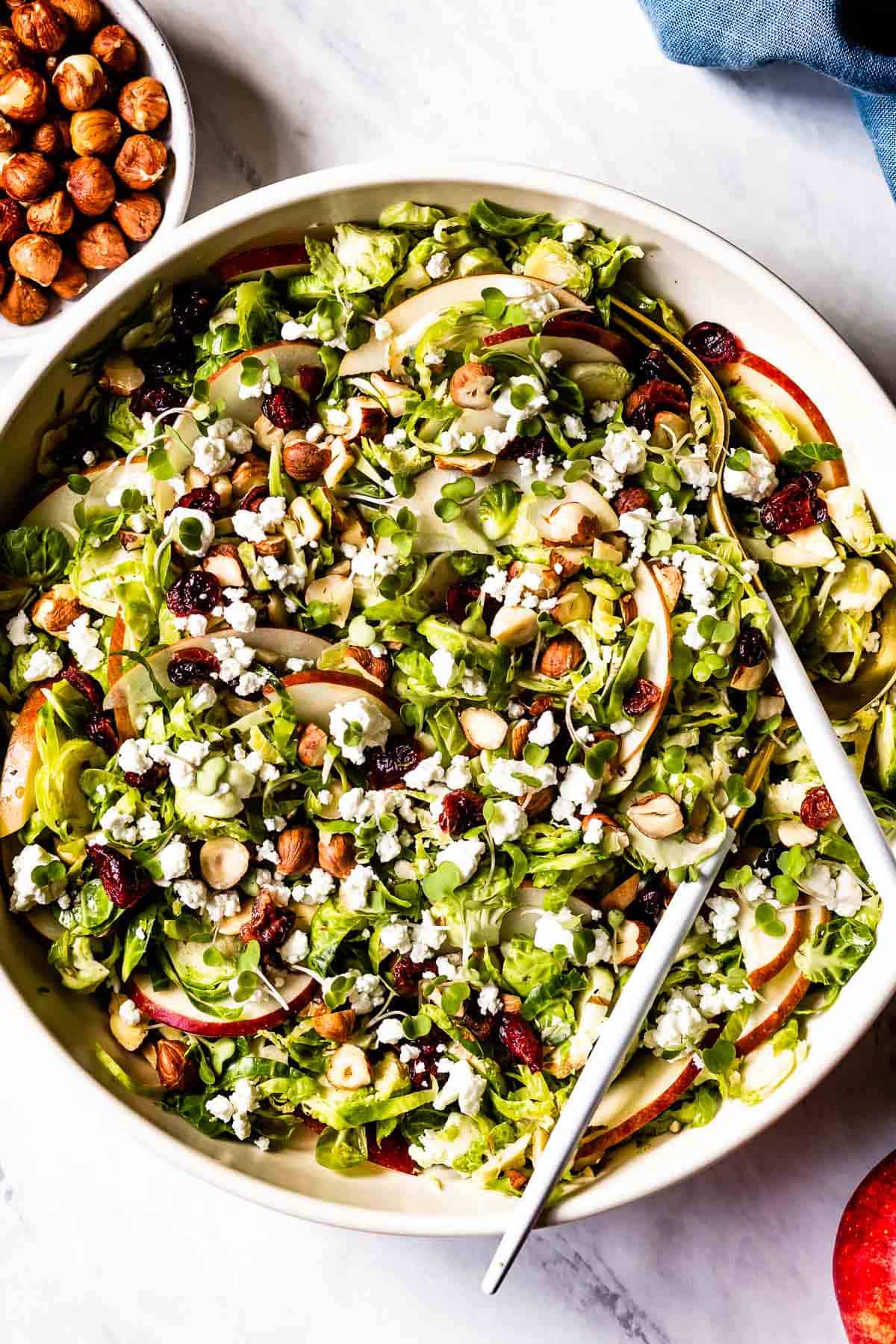 A large bowl of Shaved Brussel Sprout Salad served with hazelnuts on the side.