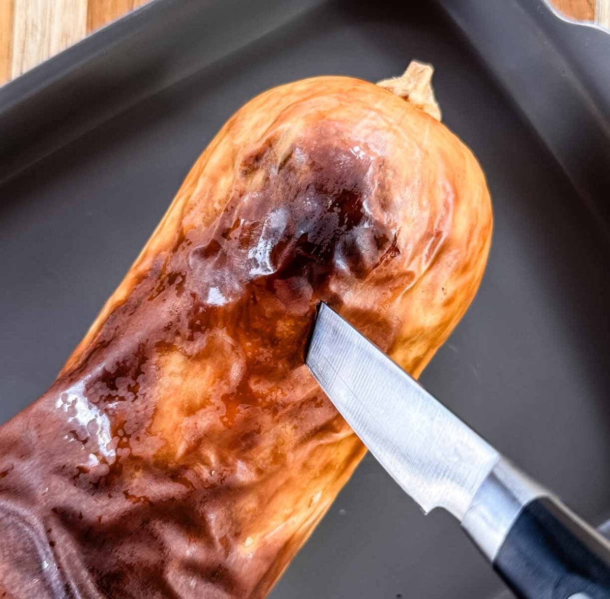 A knife inserted in the neck of a roasted whole butternut squash to check doneness.