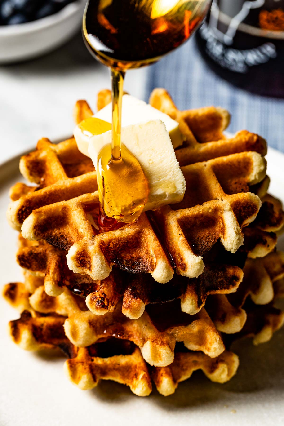 Almond flour waffles topped off with butter and being drizzled with syrup