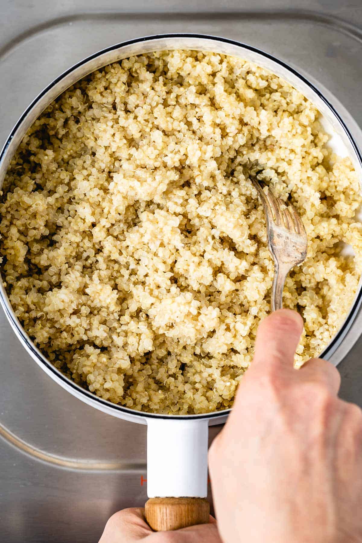 person fluffing quinoa in a saucepan