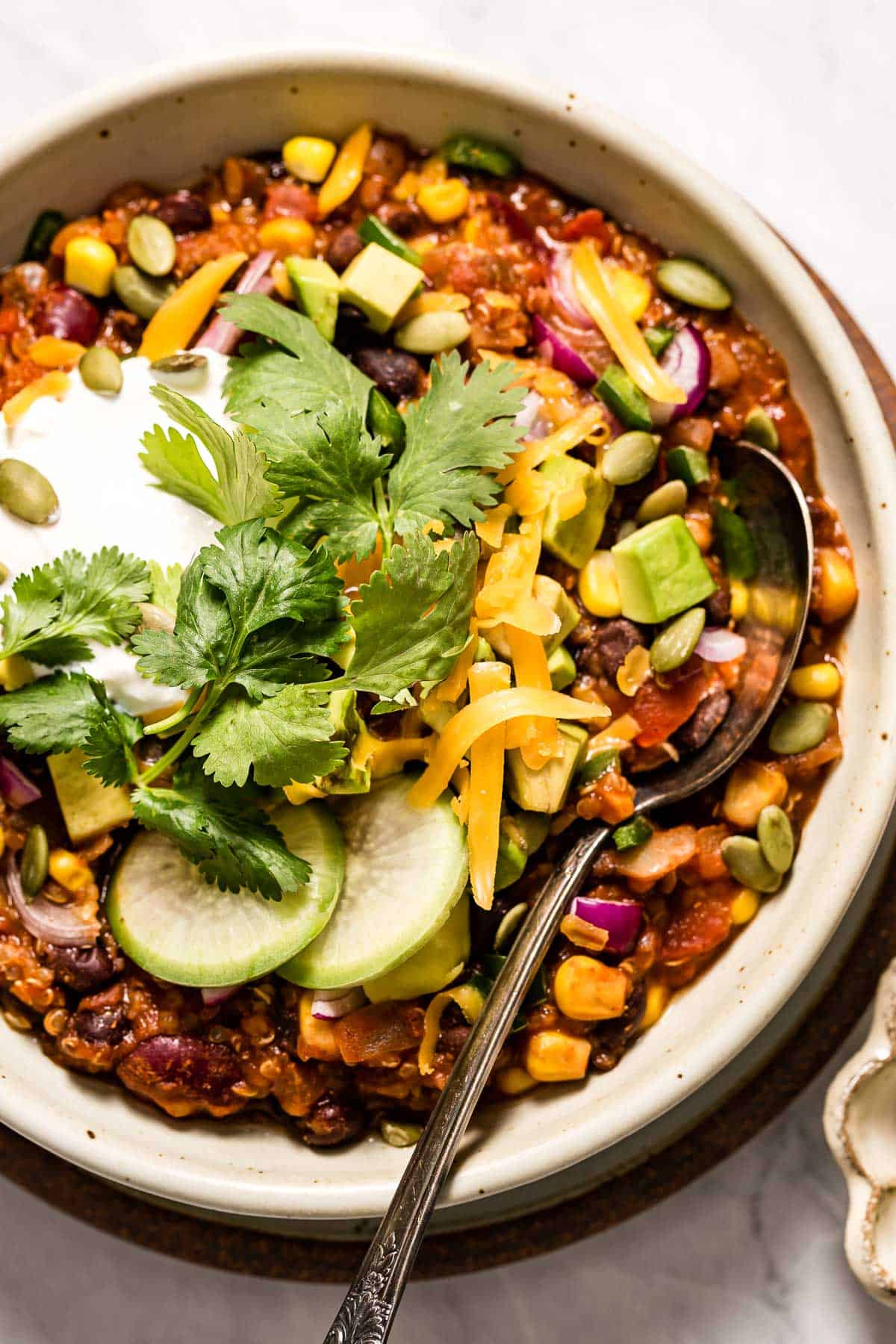 Quinoa chili topped off with chili toppings in a bowl with a spoon on the side