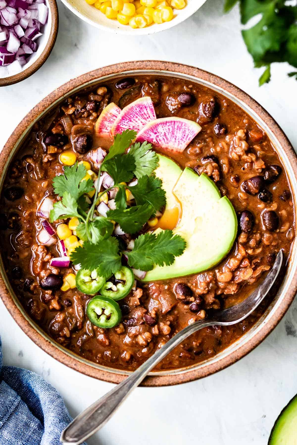 Vegan chili in a bowl garnished with cilantro and avocado slices