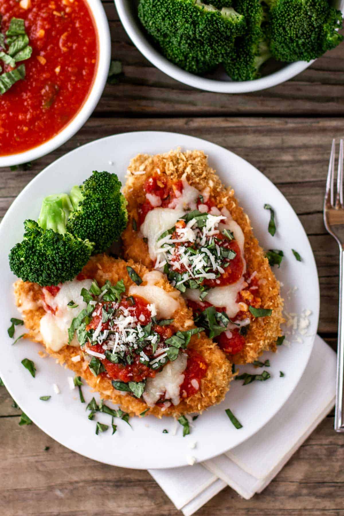Baked Chicken parmesan with roasted broccoli and marinara sauce from the top view.