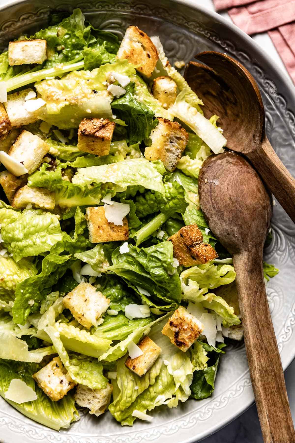 Traditional Caesar Salad in a bowl with wooden spoons on the side from the top view
