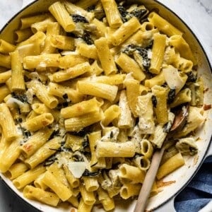 Spinach artichoke pasta bake in a skillet with a wooden spoon on the side