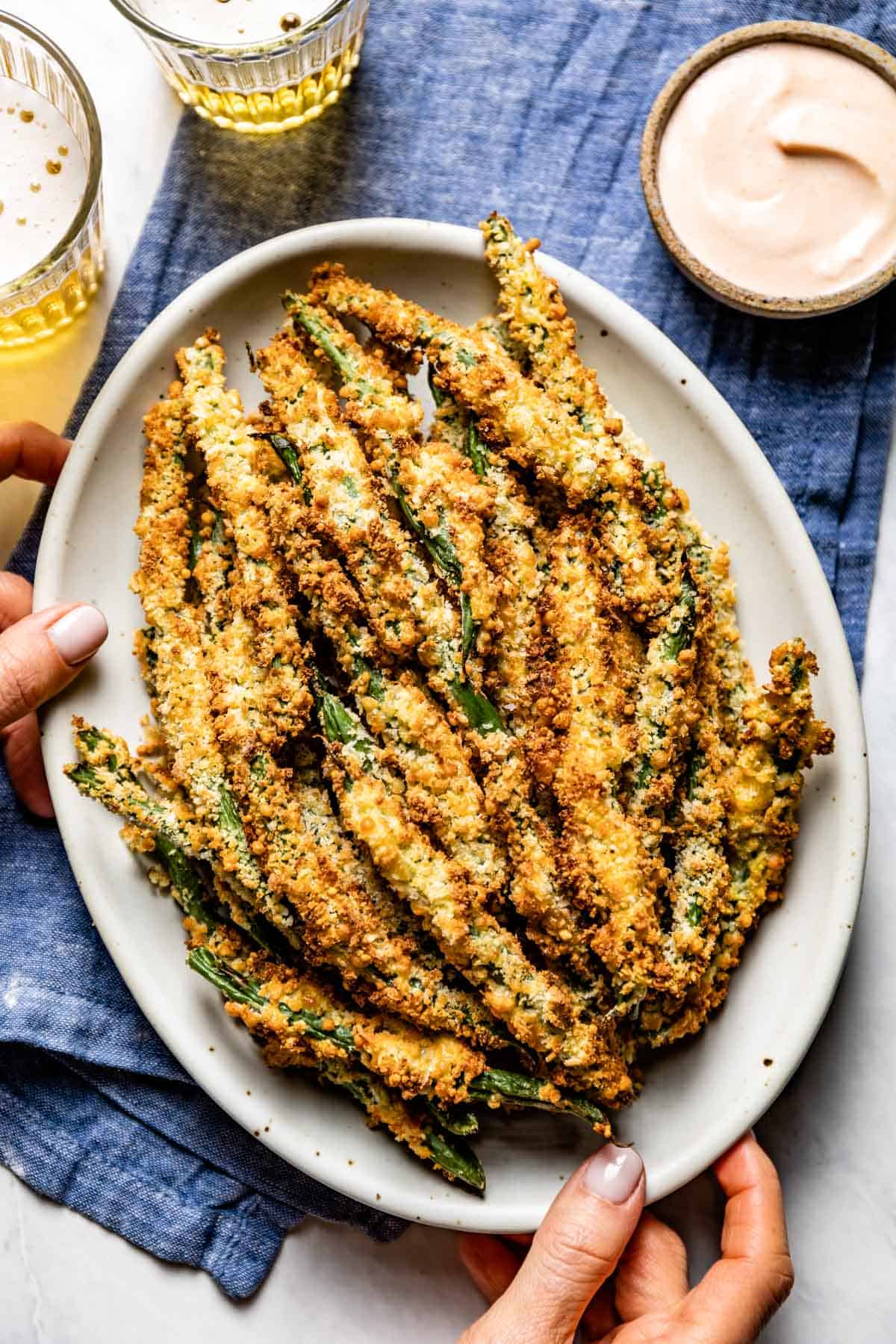 Air fried green bean fries in a plate served by a person from top view