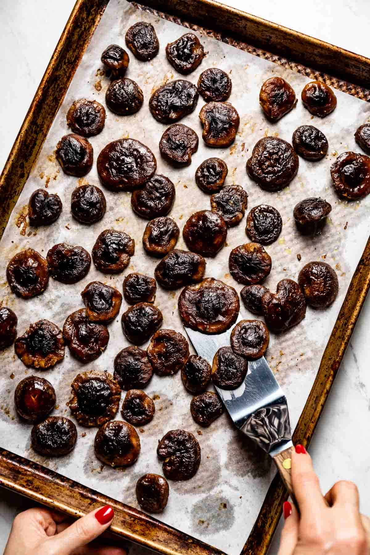 person removing roasted shiitake mushrooms from the sheet pan with a spatula