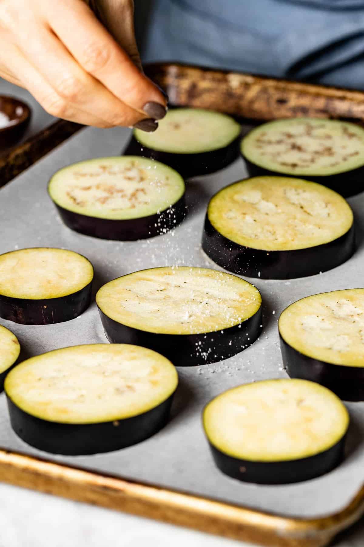 person salting eggplant slices on a sheet pan
