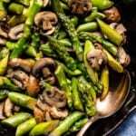 sauteed asparagus and mushrooms in a skillet with a spoon on the side