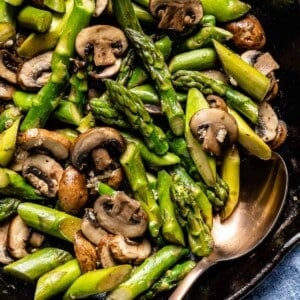 sauteed asparagus and mushrooms in a skillet with a spoon on the side