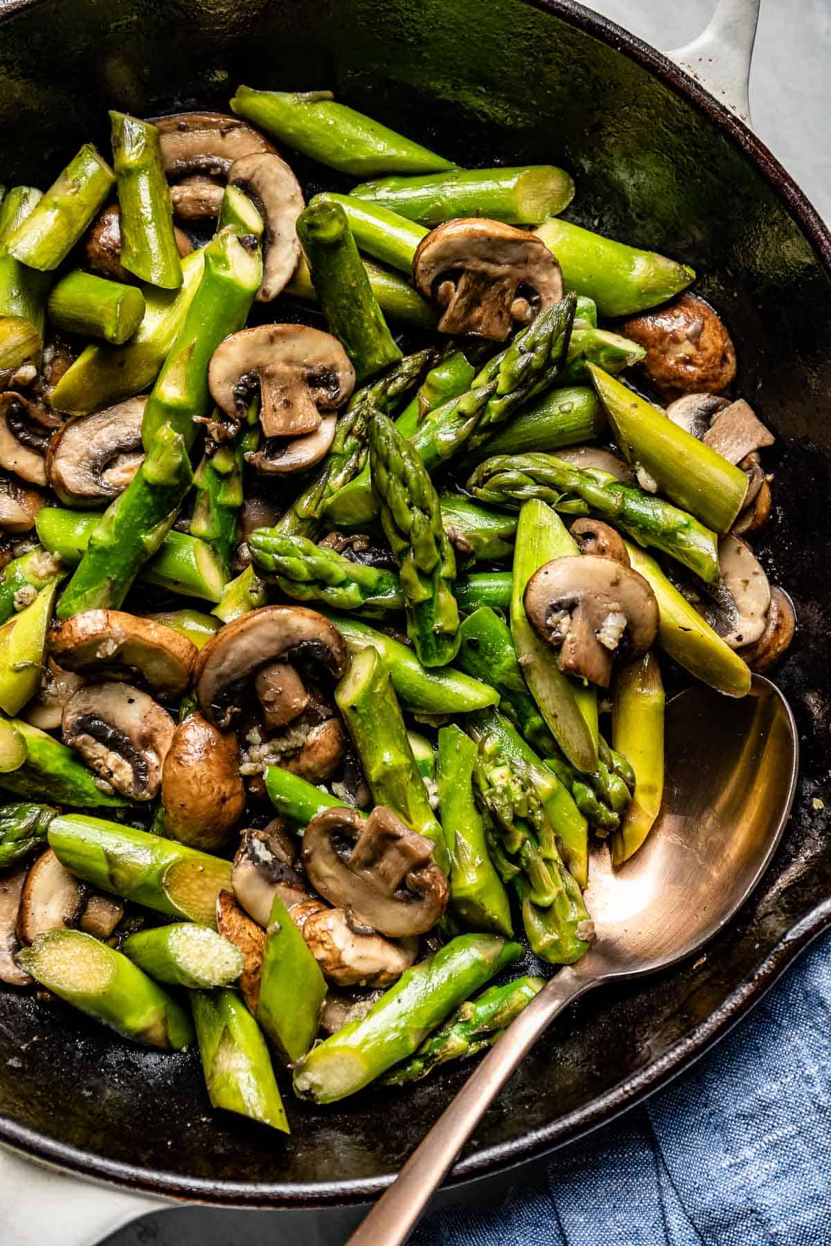 sautéed mushroom and asparagus in a cast iron skillet with a wooden spoon on the side
