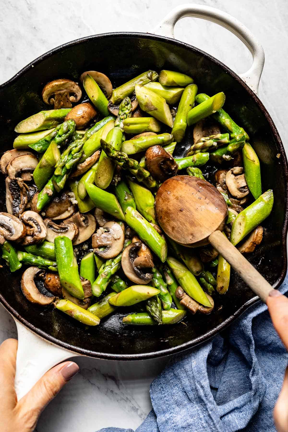 person sauteeing mushroom and asparagus in a skillet from the top view