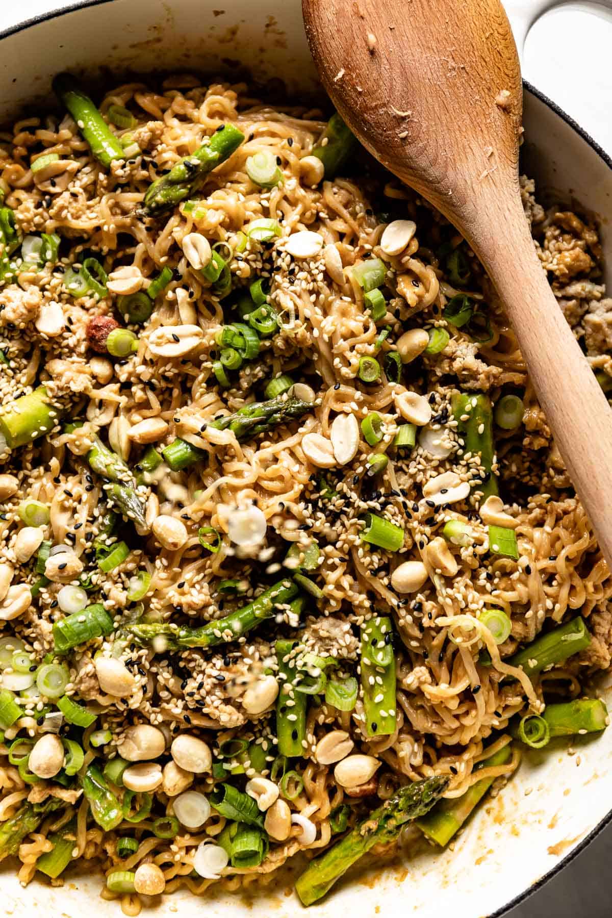 sesame noodles with chicken and asparagus in a skillet with a wooden spoon on the side