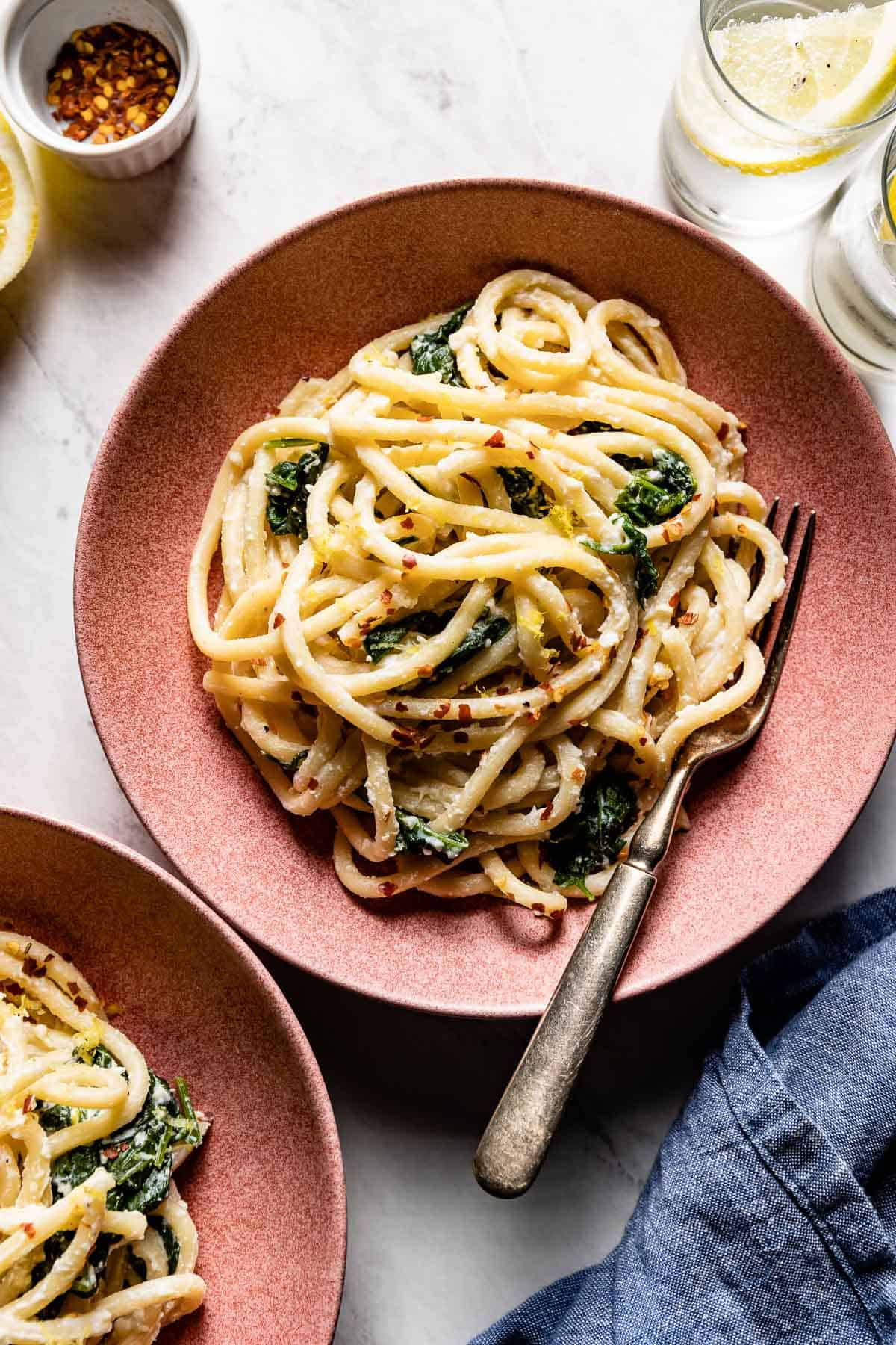 Lemon ricotta pasta in a bowl with glasses and seasoning on the side