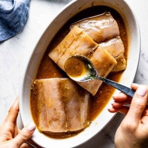 Mahi Mahi marinade in an oval bowl. A person basting fish